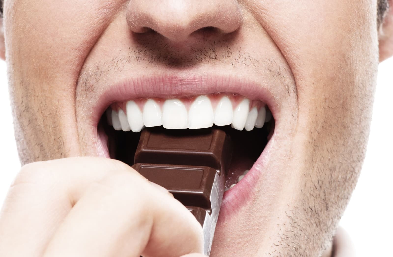 Close-up of a person's bright, white teeth as they're about to bite into a chocolate bar.