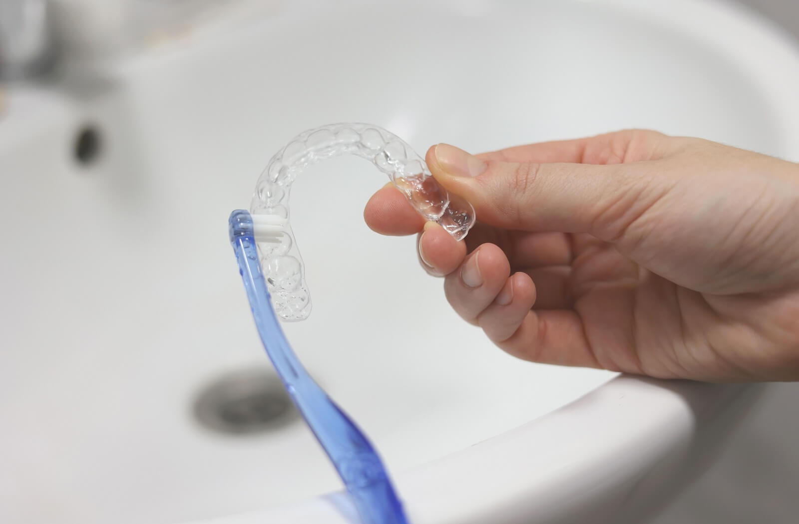 An image of someone holding their clear aligners while gently brushing them with a toothbrush.